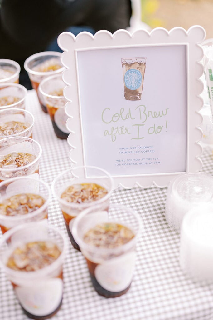 Close-up of an iced coffee wedding favor display with cups and a sign reading “Cold Brew after I do,” set up for guests after the ceremony.