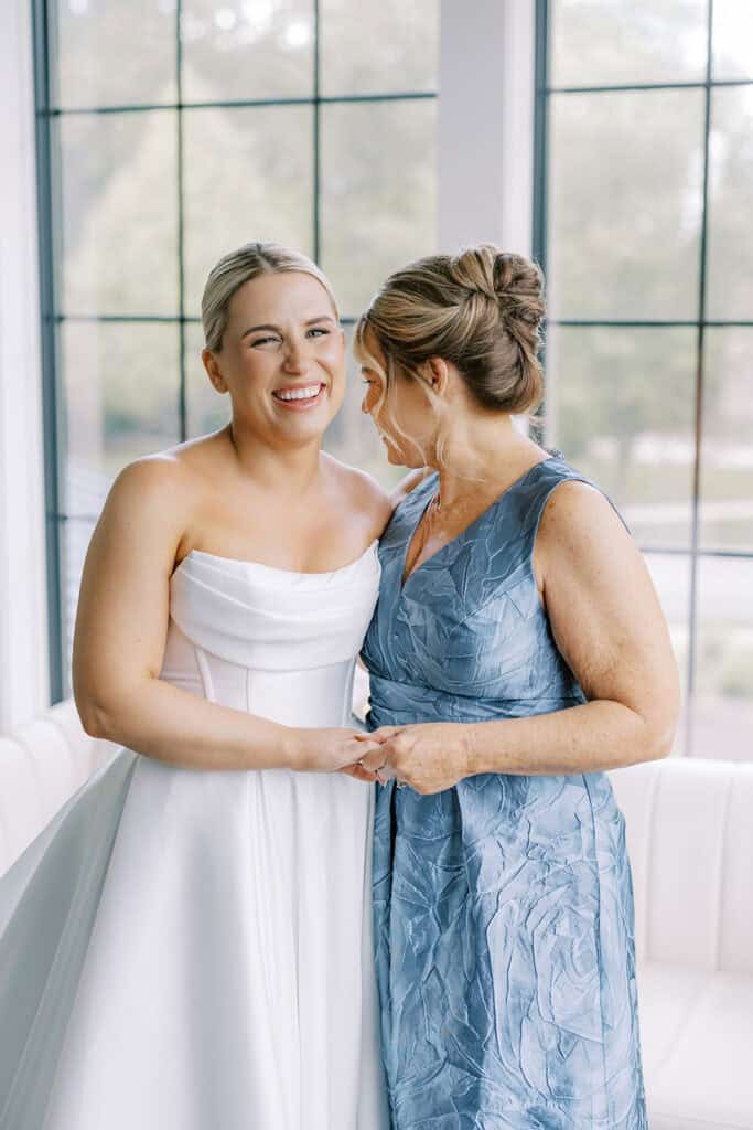 Bride smiling while holding hands with her mother in a blue dress during getting ready at The Ivy at Ellis Preserve