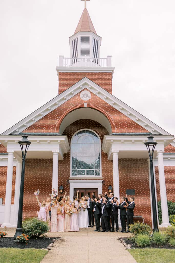 Full wedding party gathered on the steps outside Our Mother of Good Counsel Chapel at Malvern Prep, holding colorful bouquets and celebrating after the Catholic ceremony.