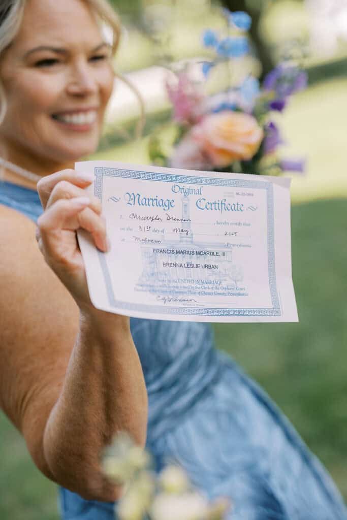 Close-up of a guest holding the signed marriage certificate for Brenna Urban and Francis McArdle outdoors, with soft greenery and florals blurred in the background.