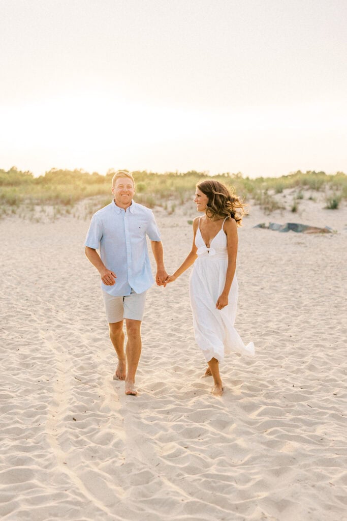 Happy couple walking on sandy beach during sunset engagement photos at Rehoboth Beach