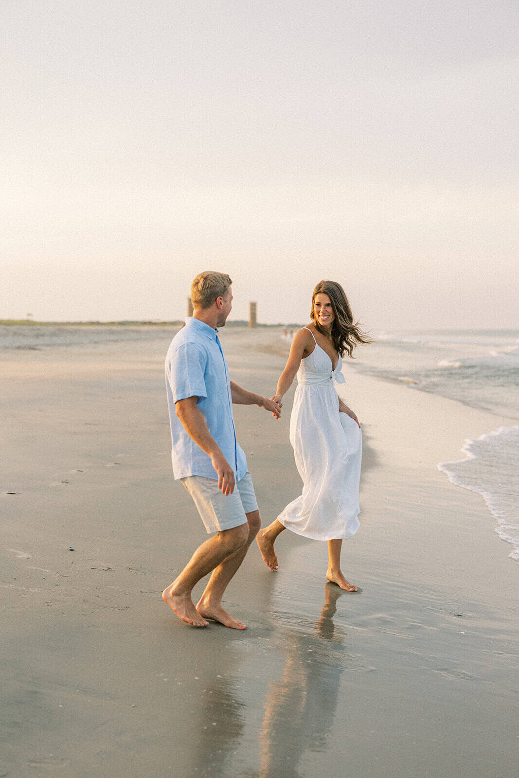Couple walking along shoreline towards the water at Rehoboth Beach Delaware engagement photoshoot