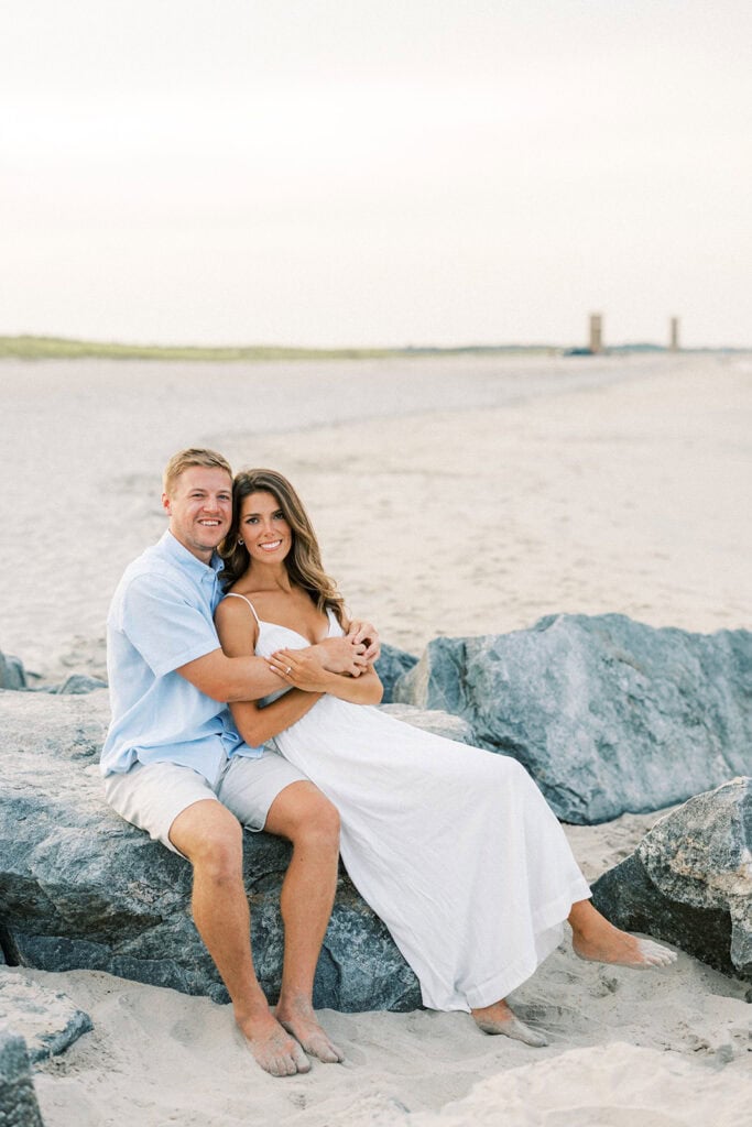 Engaged couple sitting on jetty rocks at Delaware beach engagement session