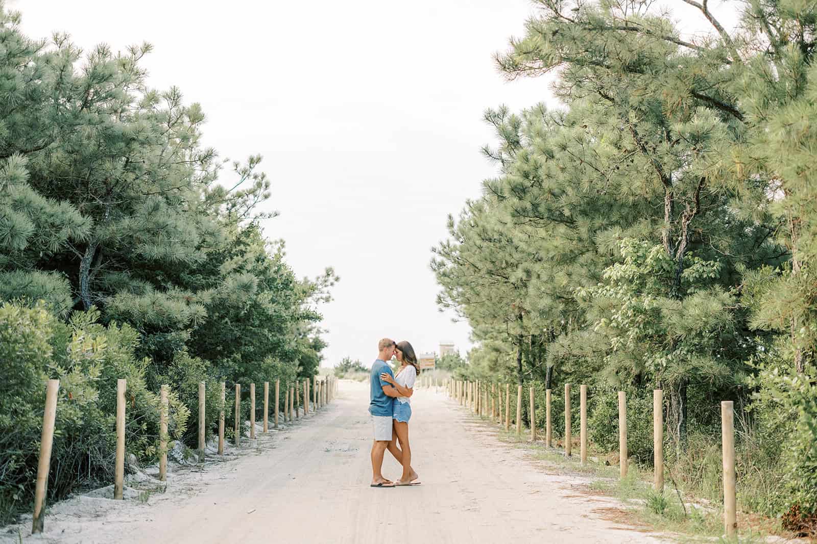 Newly engaged couple embracing on tree-lined path at Delaware beach engagement session