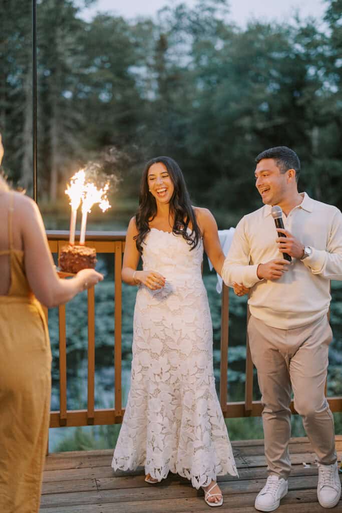 Bride and groom in rehearsal dinner attire reacting to a sparkler groom's cake surprise on the outdoor deck during their wedding weekend at Skytop Lodge in Skytop, Pennsylvania