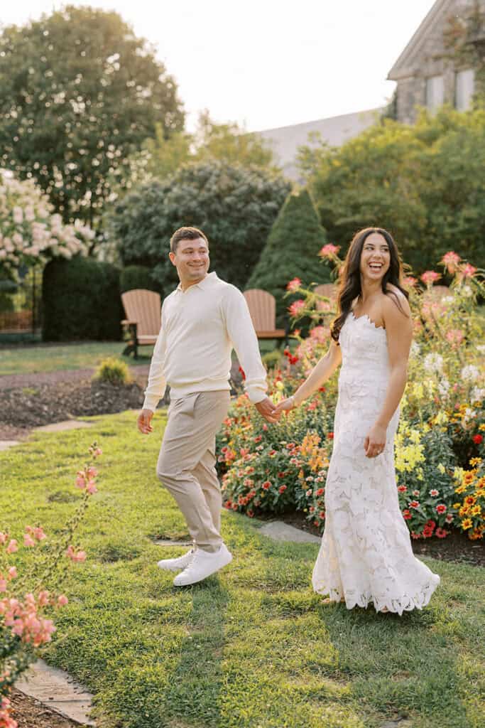 Bride and groom holding hands and walking through the colorful summer gardens at Skytop Lodge during their rehearsal dinner evening portraits and wedding weekend at Skytop