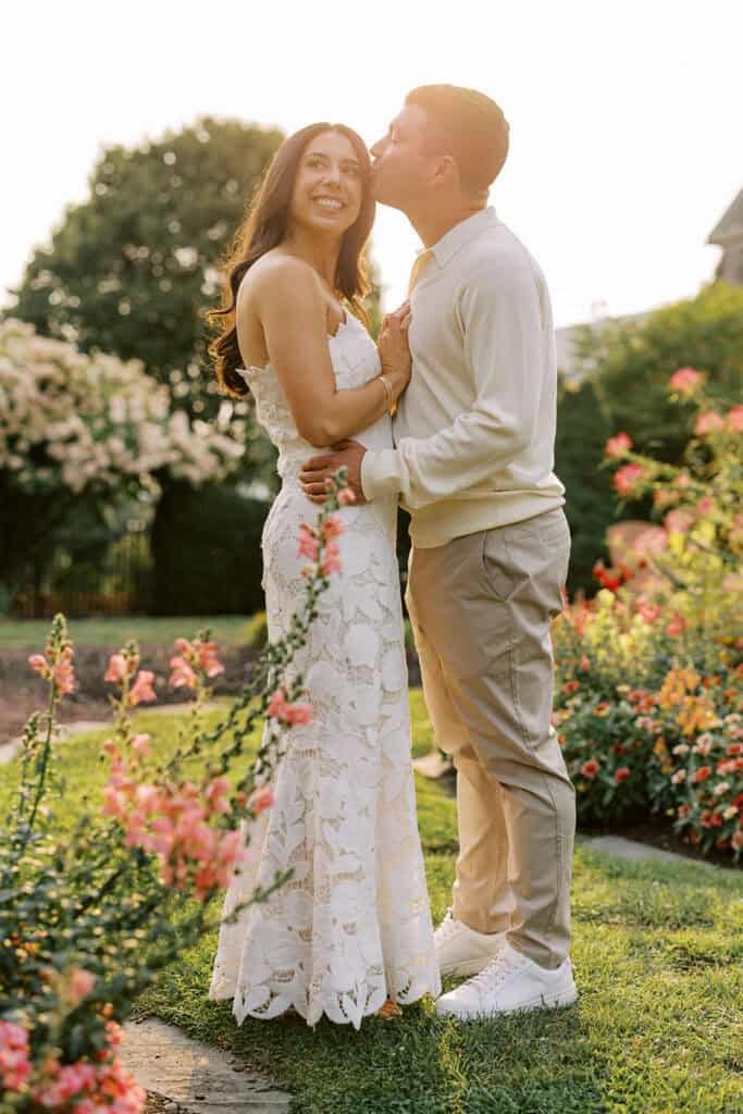 Groom kissing bride on the cheek during their wedding wedding weekend at Skytop and rehearsal dinner sunset portraits in the flower gardens at Skytop Lodge in Skytop, Pennsylvania