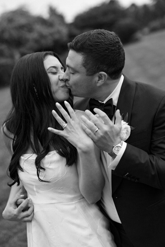 Black and white wedding day portrait of bride and groom kissing while showing their wedding rings at Skytop Lodge in Skytop, Pennsylvania