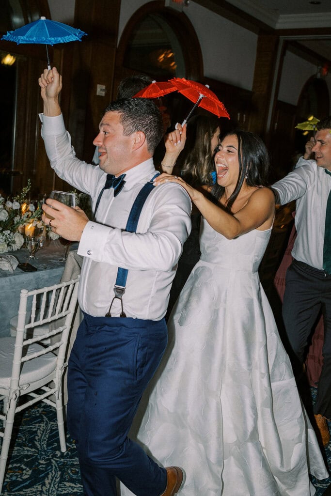 Bride and groom dancing joyfully with colorful cocktail parasols during their wedding reception at Skytop Lodge in the Pocono Mountains