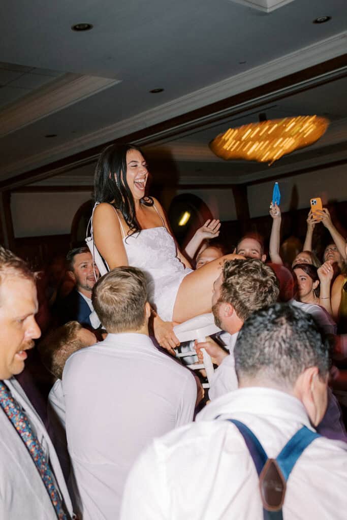 Bride lifted on a chair by wedding guests during a joyful hora dance at a Skytop Lodge wedding reception in Skytop, Pennsylvania