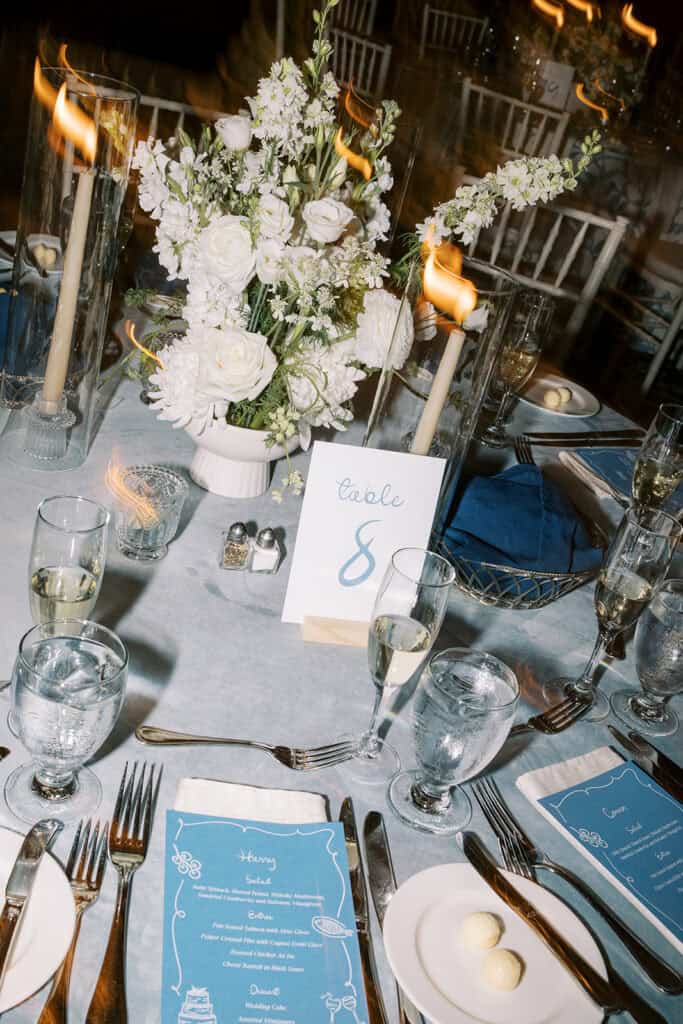 Round reception table detail with blue personalized menu cards, white floral centerpiece, taper candles, and dusty blue linens at a Skytop Lodge wedding in Skytop, Pennsylvania