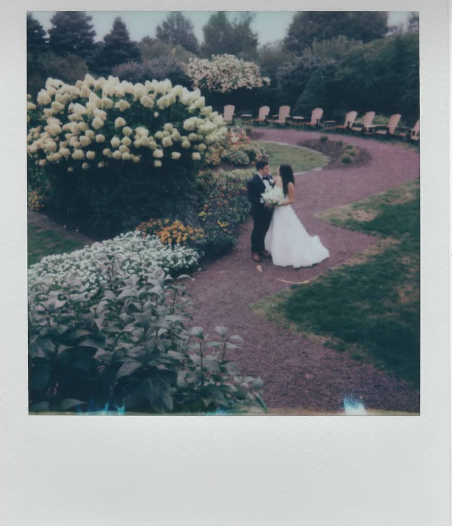 Polaroid of bride and groom sharing a moment on the winding garden path surrounded by hydrangeas and summer blooms at Skytop Lodge in Skytop, Pennsylvania