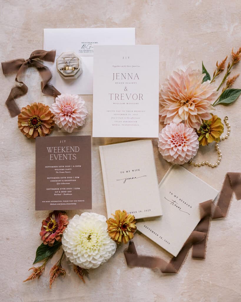 Jenna and Trevor wedding invitation suite flatlay with vow books, engagement ring, pearl bracelet, and fall dahlias and zinnias, Tyler Arboretum Media Pennsylvania September 2025