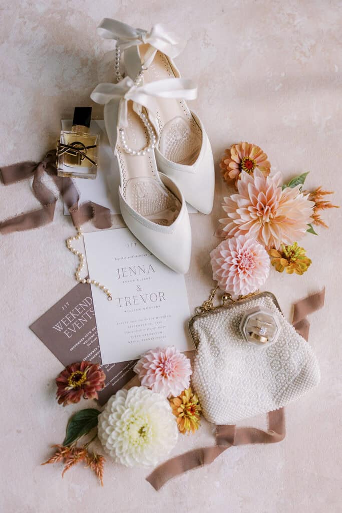 Bridal details flatlay with white pointed-toe heels with pearl ankle straps, pearl clutch, Minted wedding invitation suite, and fall floral blooms, Tyler Arboretum wedding Media PA