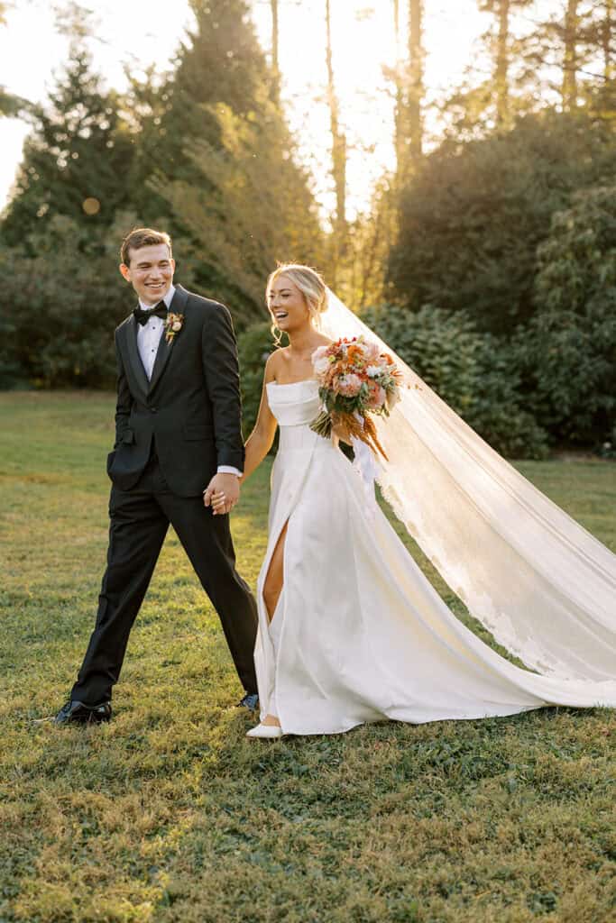 Bride and groom laughing together at golden hour in the Tyler Arboretum gardens, bride's cathedral veil flowing behind her in strapless gown with fall bouquet, Philadelphia wedding photographer Samantha Jay Photo