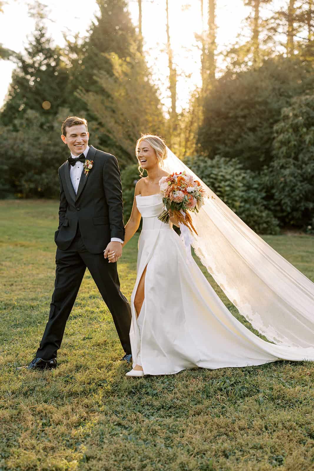 Bride and groom laughing together at golden hour in the Tyler Arboretum gardens, bride's cathedral veil flowing behind her in strapless gown with fall bouquet, Philadelphia wedding photographer Samantha Jay Photo