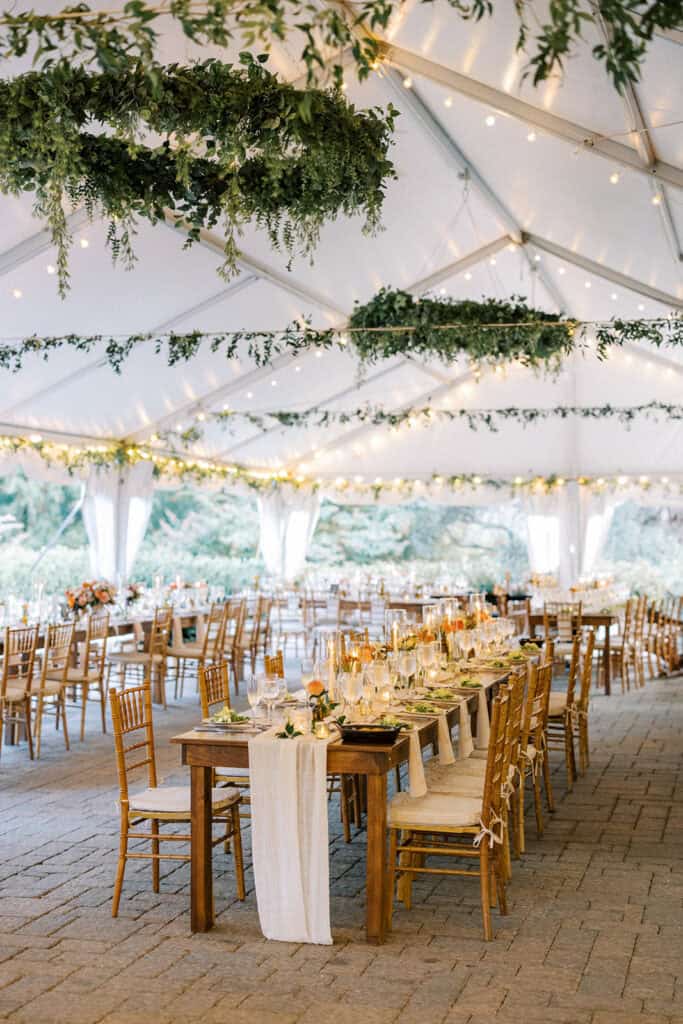 Full view of Tyler Arboretum tented wedding reception with hanging greenery chandeliers, string lights, farm tables with lace runners and fall floral centerpieces, photographed by Samantha Jay Photo