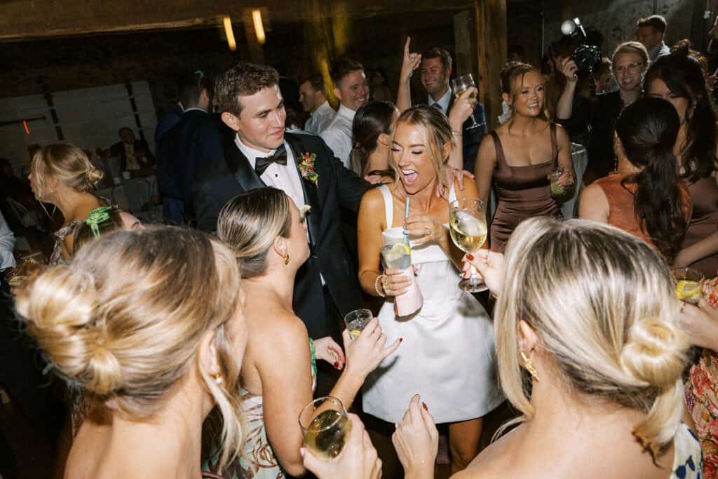 Bride in short white reception dress laughing on the dance floor at Tyler Arboretum barn wedding with guests and groom celebrating, fall wedding photography Media PA