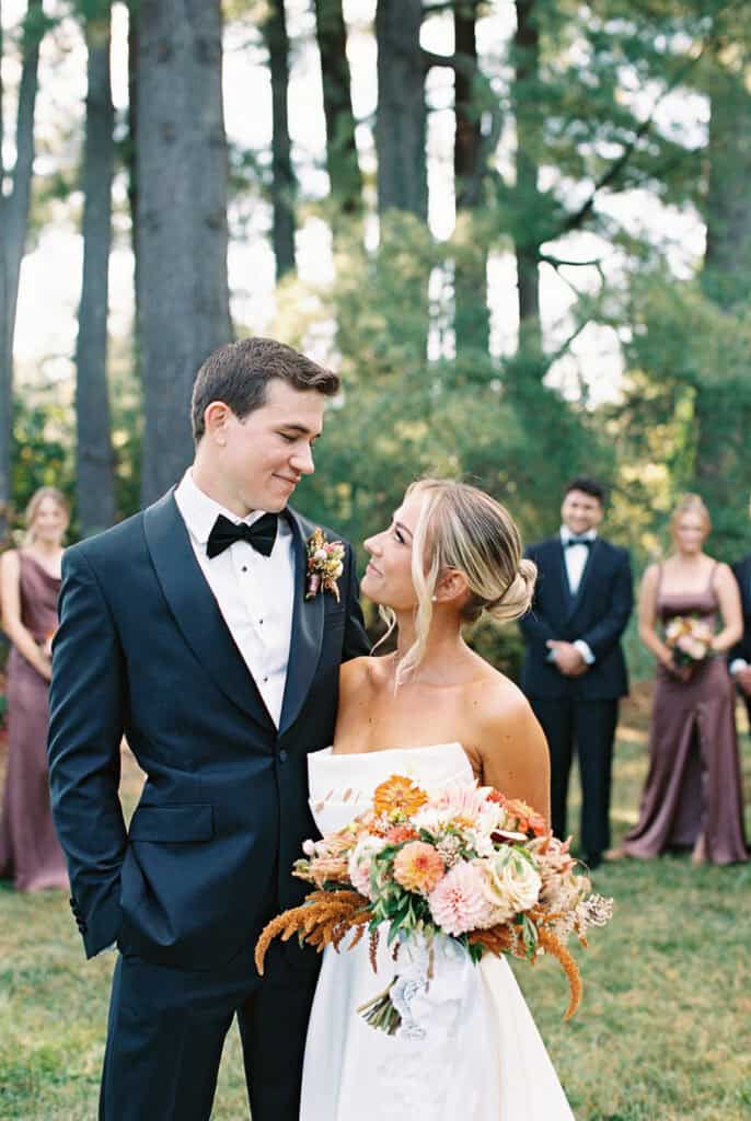 Bride and groom sharing a quiet moment with wedding party in the background at Tyler Arboretum, bridesmaids in chocolate brown gowns, fall film wedding photography