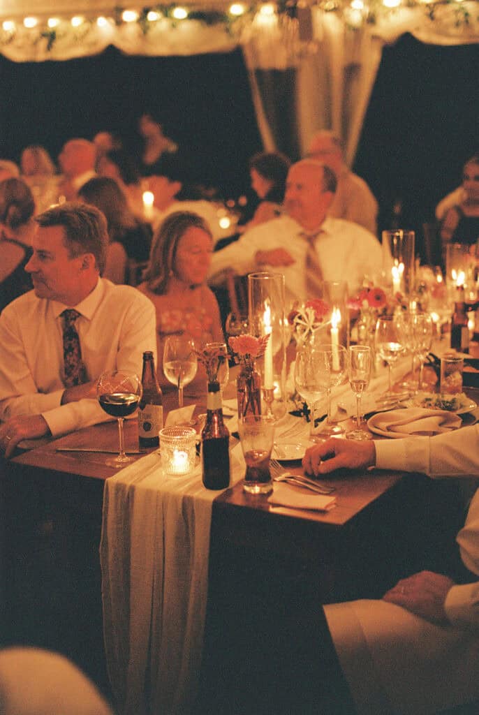 Candlelit tented wedding reception at Tyler Arboretum with string lights, long tables, linen runners, and taper candles, photographed on film