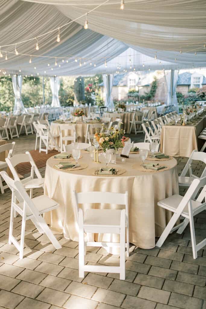 Draped tent reception setup with string lights champagne linens and wildflower centerpieces at Drumore Estate summer wedding venue Lancaster PA