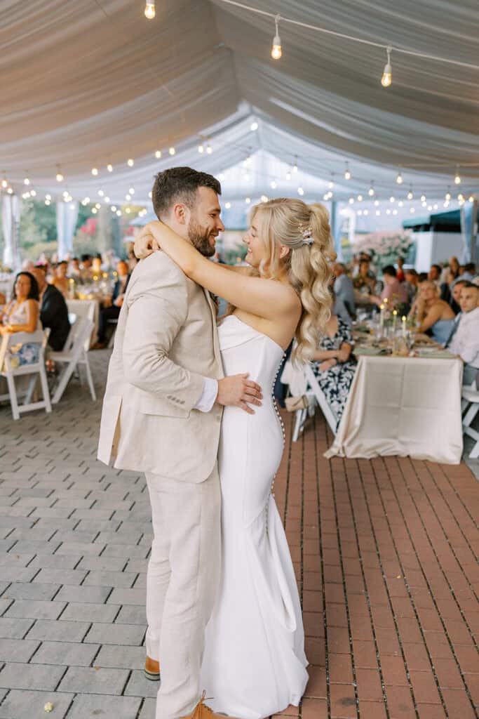 Bride and groom sharing first dance under string lights inside Drumore Estate Grand Tent at summer wedding in Lancaster County Pennsylvania