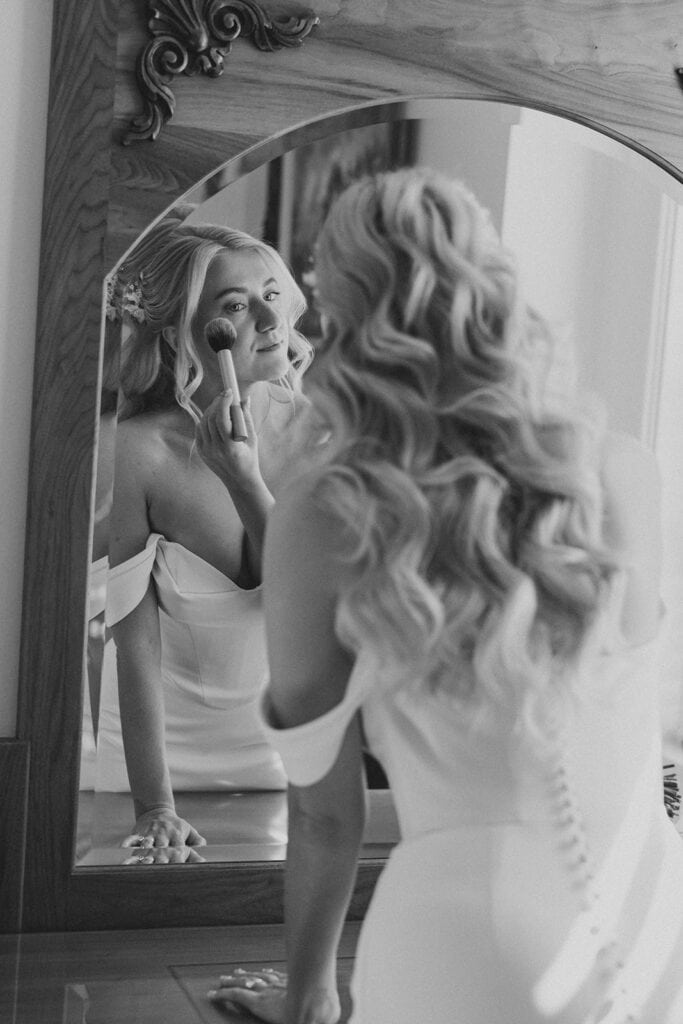 Black and white mirror reflection of bride applying makeup during getting ready at Drumore Estate summer wedding in Lancaster County Pennsylvania