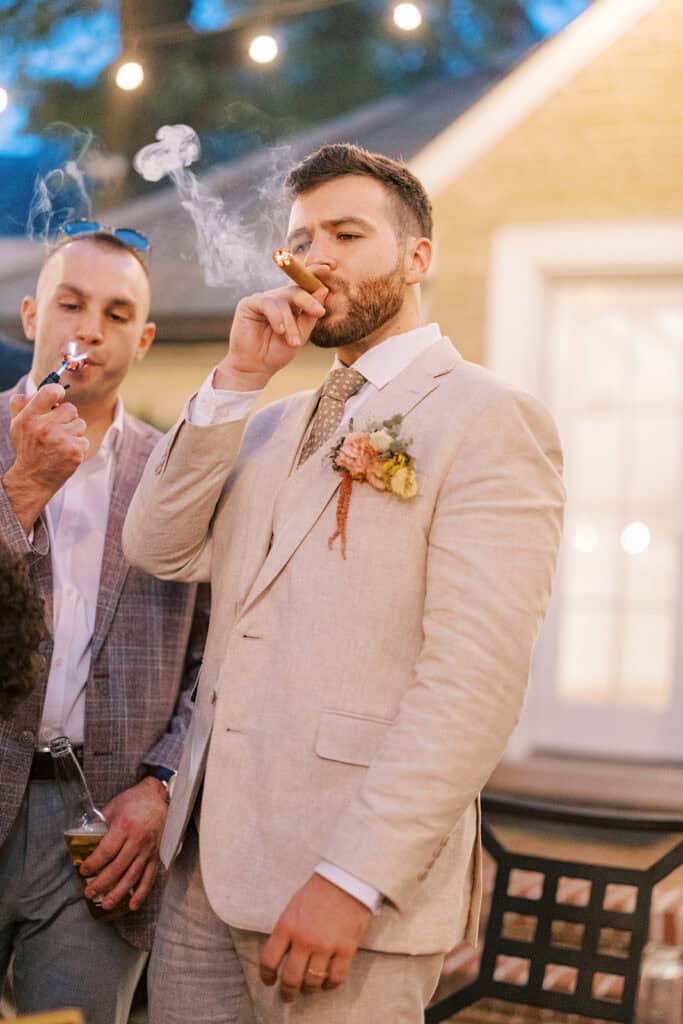 Groom smoking cigar with guests during evening reception at Drumore Estate outdoor summer wedding in Pequea Lancaster County PA