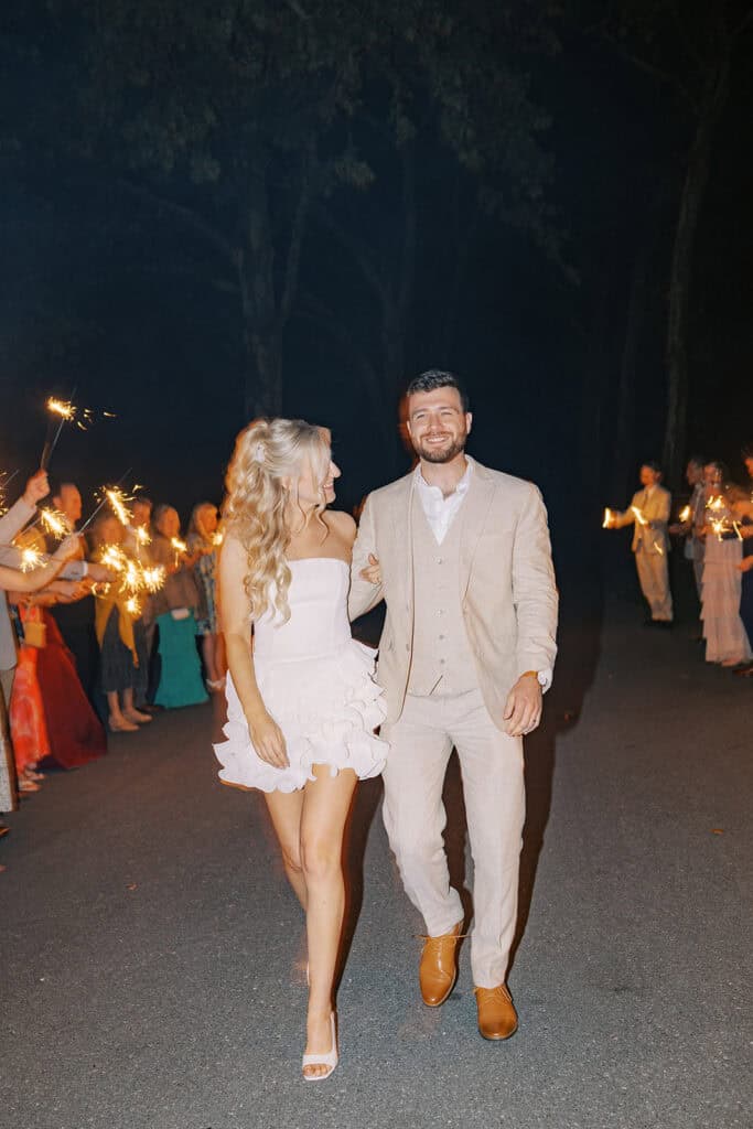 Bride in white ruffle mini dress and groom smiling during sparkler exit at Drumore Estate outdoor summer wedding in Pequea Pennsylvania