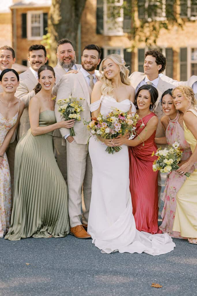Full wedding party portrait with bride in Madi Lane gown and bridesmaids in mixed color dresses holding wildflower bouquets at Drumore Estate summer wedding