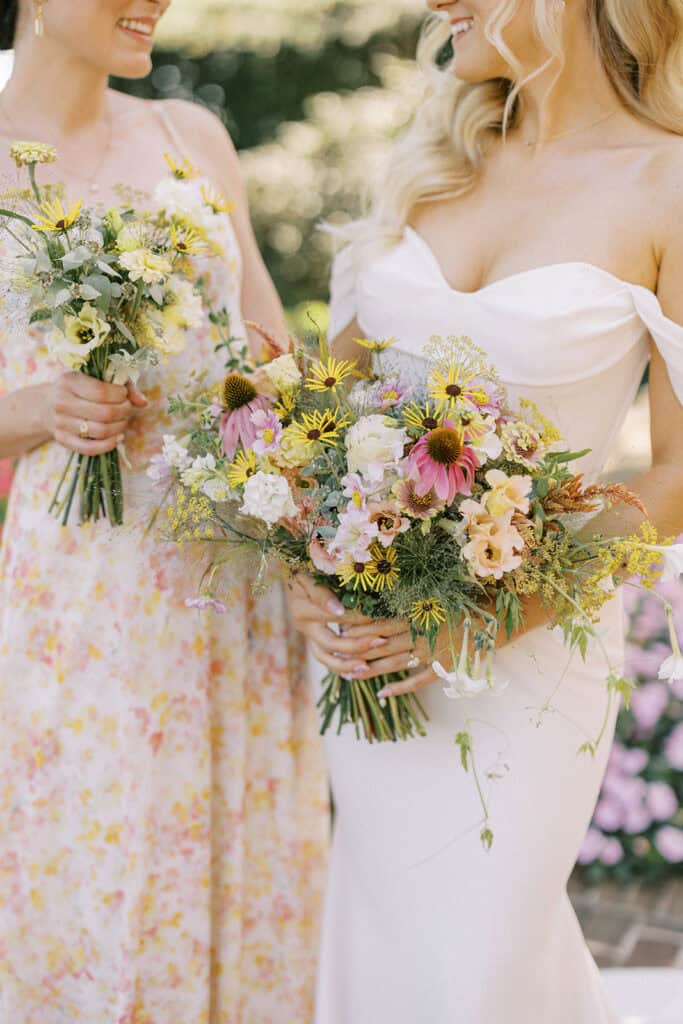 Close-up of bride and bridesmaid holding wildflower bouquets with yellow daisies and pink coneflowers at Drumore Estate summer wedding in Pequea PA