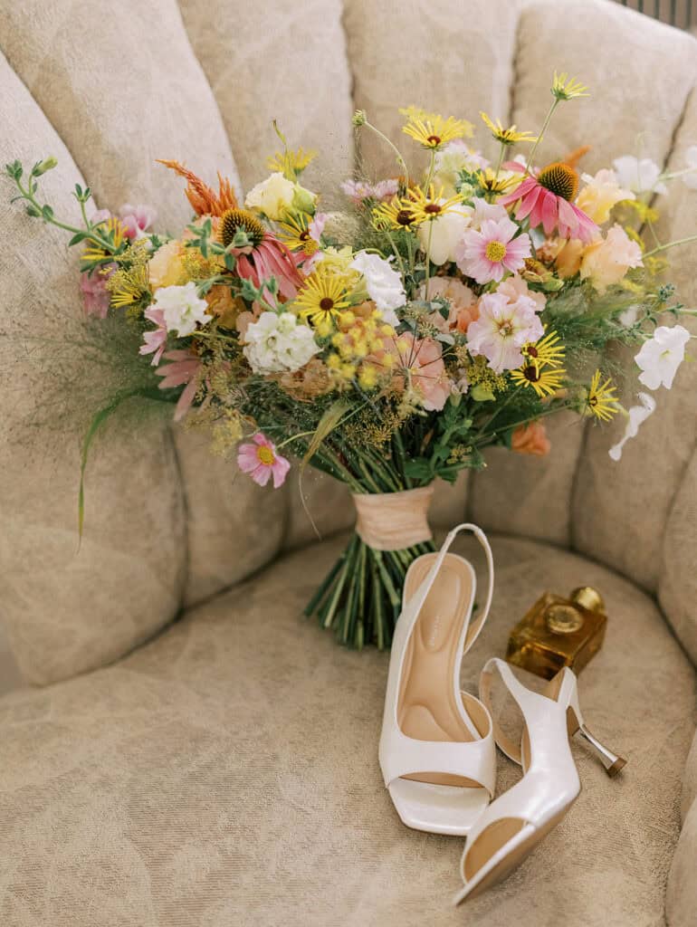 Bright wildflower bridal bouquet with pink coneflowers and yellow daisies beside white bridal heels during summer wedding getting ready at Drumore Estate