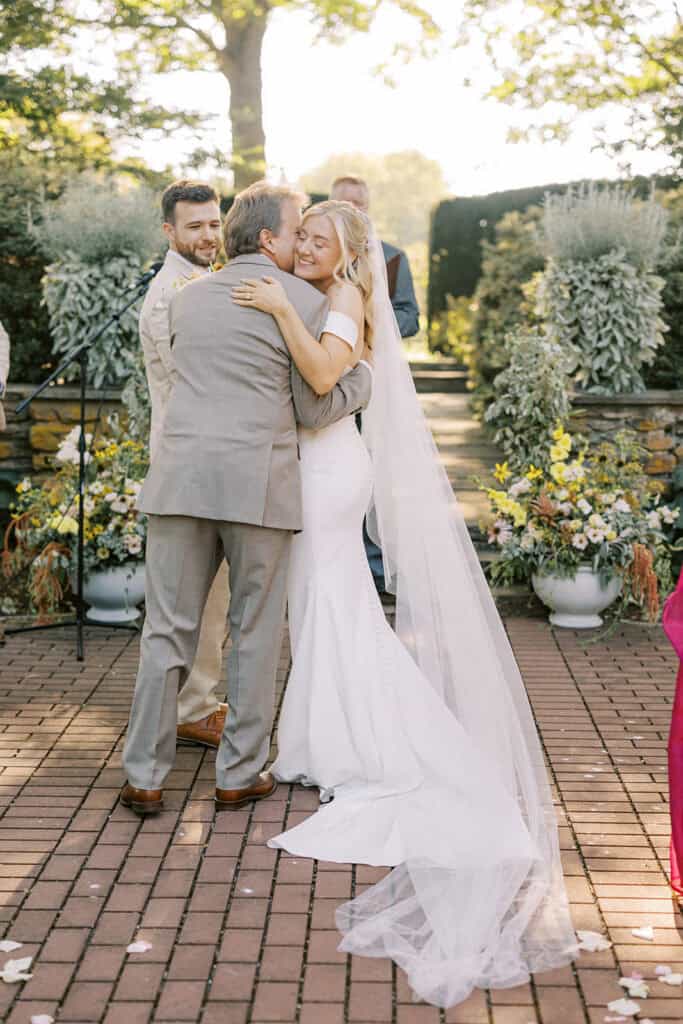 Bride hugging father at altar after being given away at Drumore Estate outdoor summer wedding ceremony in Pequea Lancaster County PA
