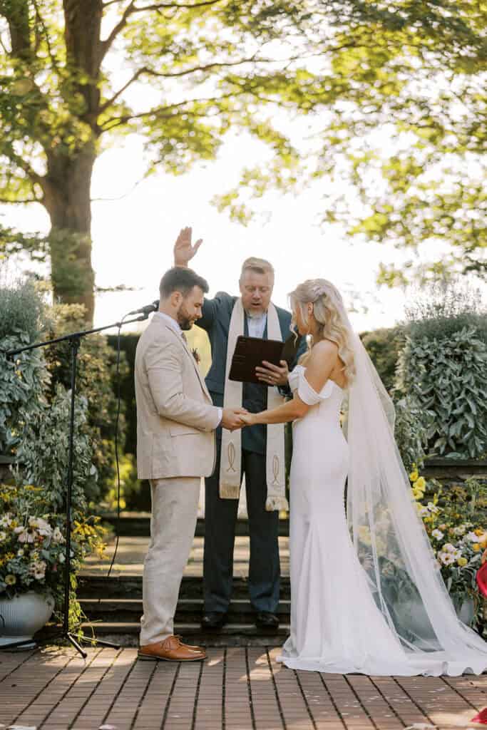Bride and groom exchanging vows with officiant at outdoor Drumore Estate wedding ceremony surrounded by summer wildflower arrangements
