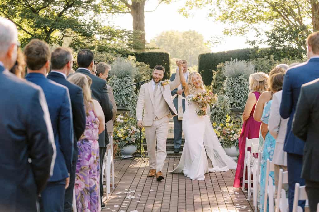 Bride and groom walking back down the aisle after ceremony at Drumore Estate summer wedding in Lancaster PA with hands raised in celebration