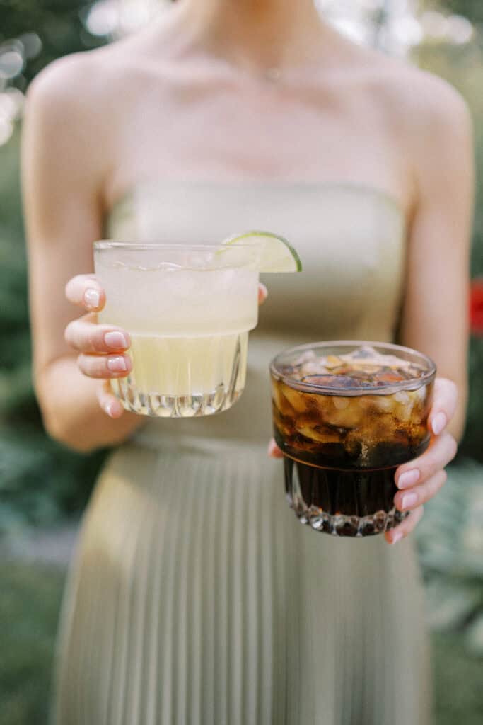Bridesmaid holding two cocktail glasses at Drumore Estate summer wedding cocktail hour in Pequea Lancaster County Pennsylvania