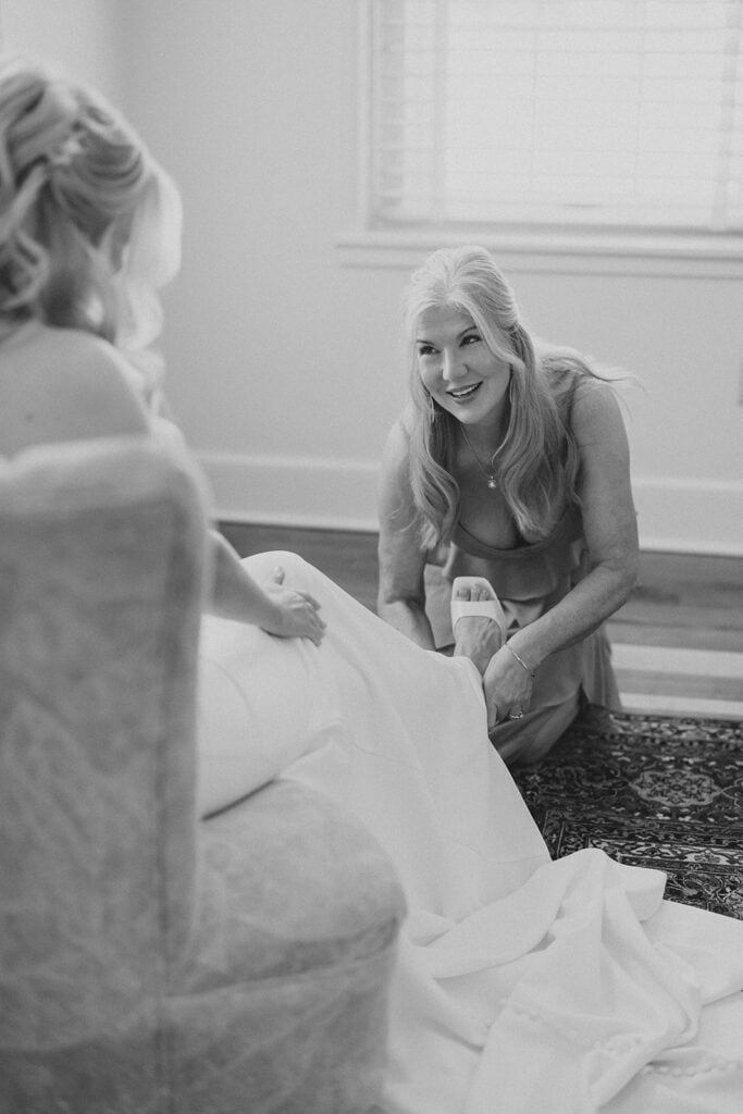 Black and white photo of mother of the bride helping bride with shoes during getting ready at Drumore Estate summer wedding in Pequea PA