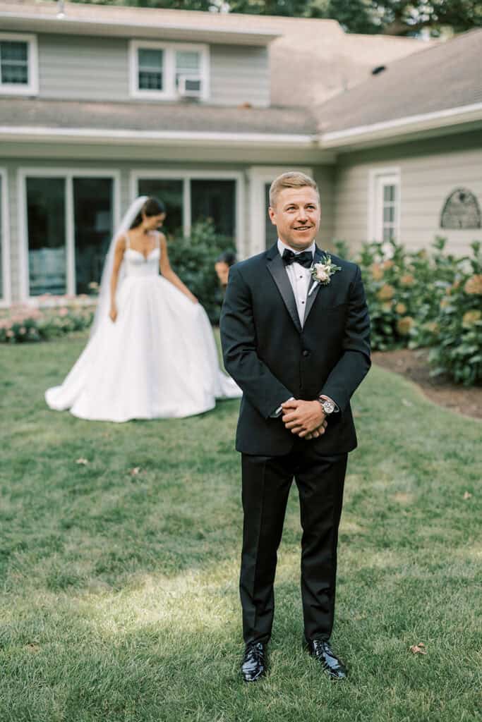 Groom waiting and smiling during first look with bride approaching in background, Rehoboth Beach Delaware wedding photography