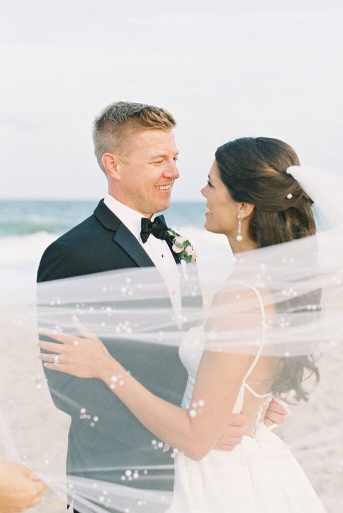 Veil wrapping around bride and groom at the ocean's edge during their Rehoboth Beach wedding, film photography