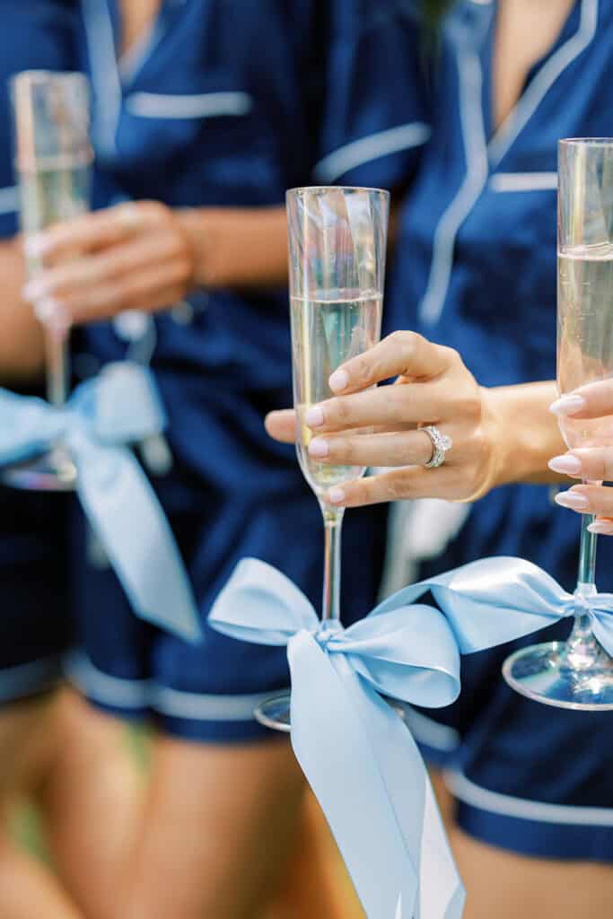 Bridesmaids in navy satin pajamas toasting champagne with blue ribbon flutes during Rehoboth Beach wedding morning getting ready