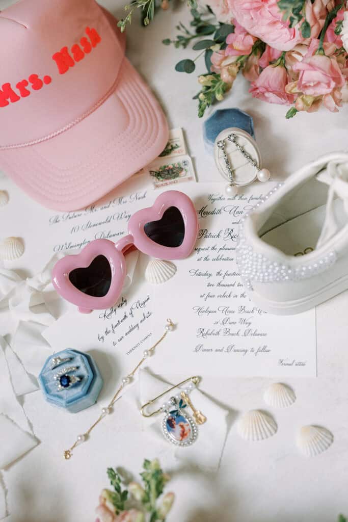 Bride getting ready details flat lay with Mrs. Nash trucker hat, heart sunglasses, pearl sneakers, and sapphire ring at Rehoboth Beach wedding