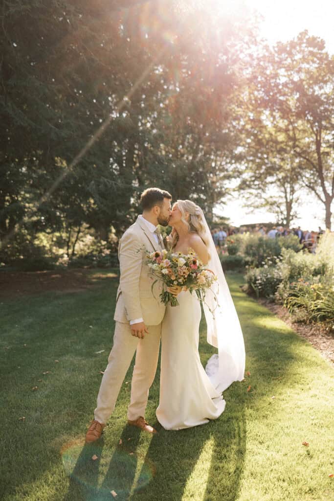 Bride and groom first kiss after outdoor ceremony at Drumore Estate summer wedding with wildflower bouquet and late afternoon sun flare