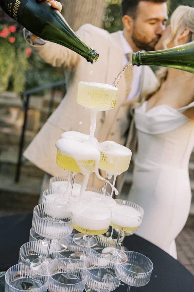 Champagne tower being poured at Drumore Estate wedding cocktail hour with bride and groom kissing in the background