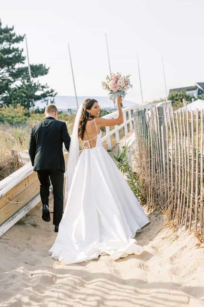 Bride raising bouquet along beach boardwalk after Rehoboth Beach wedding ceremony at Henlopen Acres Beach Club, Delaware
