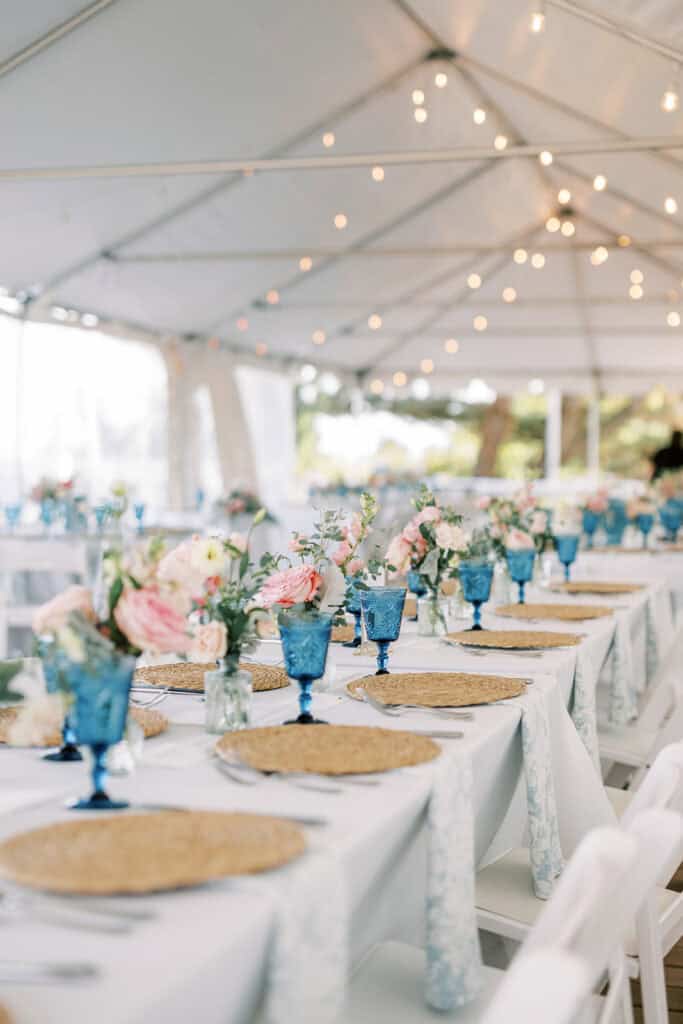 Tented wedding reception tablescape at Henlopen Acres Beach Club with blue goblets, rattan chargers, and blush floral centerpieces, Rehoboth Beach Delaware