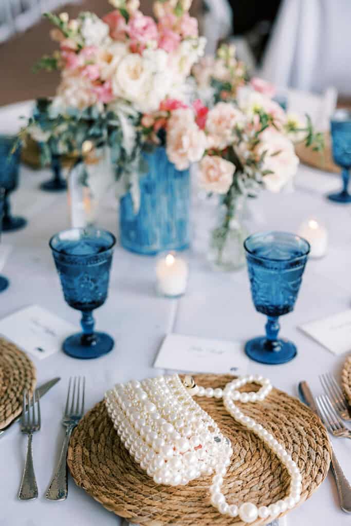Beach wedding reception place setting with pearl clutch, rattan charger, and blue goblets at Henlopen Acres Beach Club Rehoboth Beach Delaware