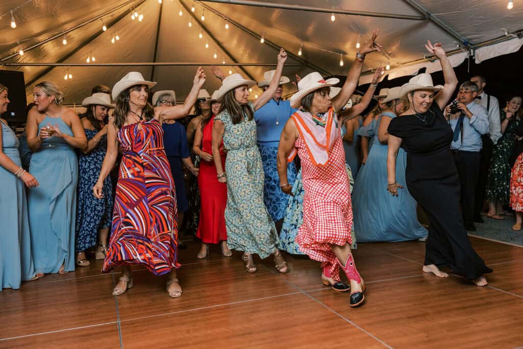Wedding guests line dancing in cowboy hats under string lights at Henlopen Acres Beach Club reception, Rehoboth Beach Delaware