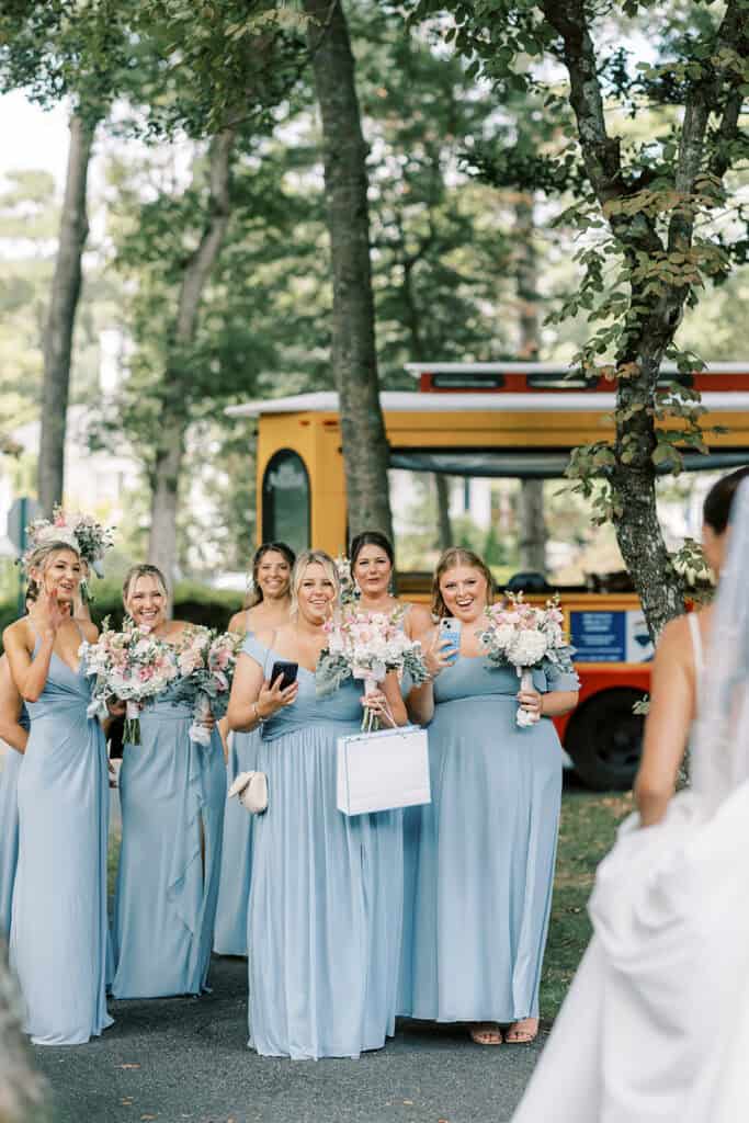 Bridesmaids in dusty blue gowns reacting to bride's arrival with blush bouquets at Rehoboth Beach Delaware wedding