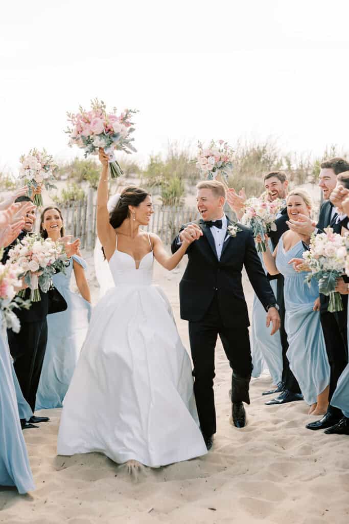 Wedding party celebrating with bride and groom on Rehoboth Beach with blush and dusty blue bouquets, Delaware wedding photography