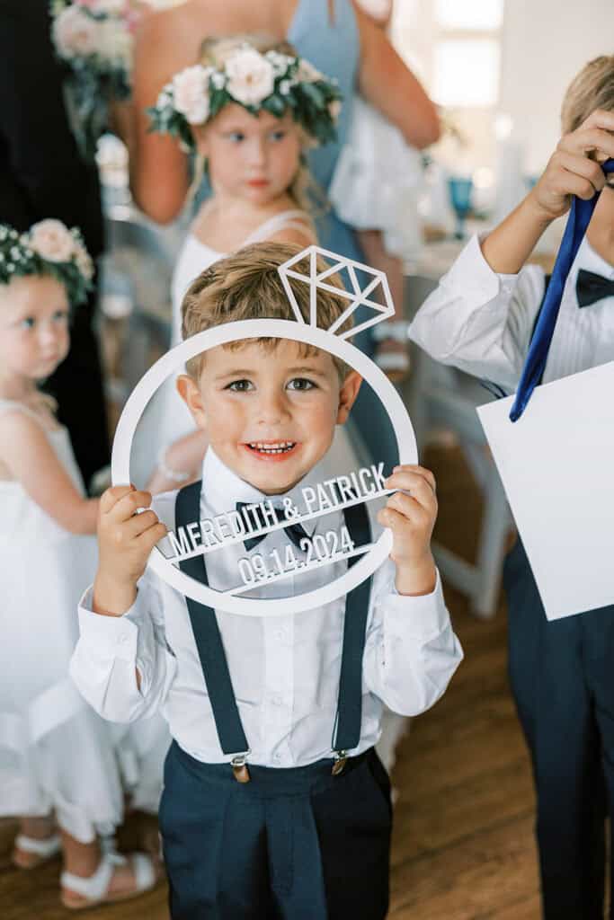 Ring bearer holding custom Meredith and Patrick wedding sign at Rehoboth Beach ceremony, Henlopen Acres Beach Club Delaware
